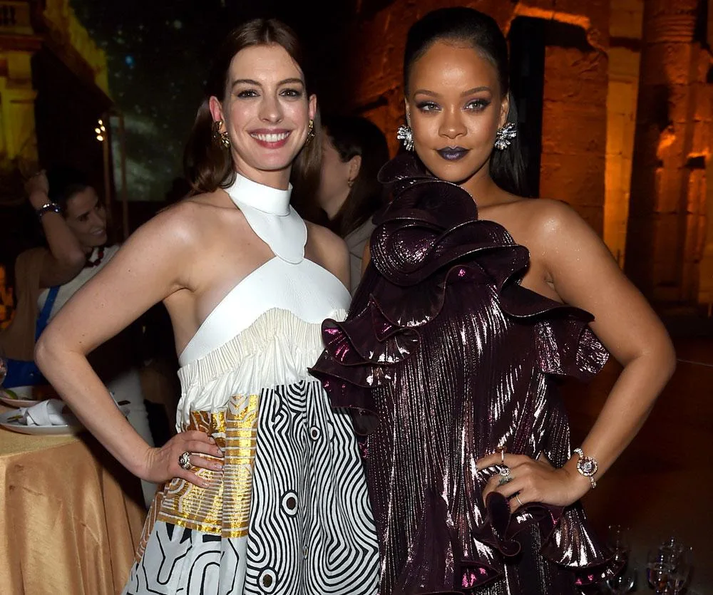 Anne Hathaway and Rihanna in stylish dresses smile and pose together at a formal event.