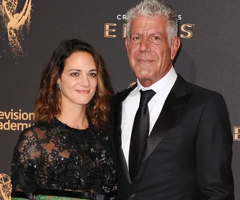 Two individuals pose together, dressed formally, in front of a "Television Academy Emmys" backdrop.