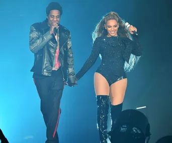 Two performers, holding hands, on stage in a concert with blue lighting.