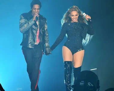 Two performers, holding hands, on stage in a concert with blue lighting.