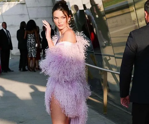 Woman in a fluffy feather dress waves at an event while walking past others in formal attire.