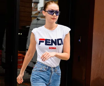 Gigi Hadid wearing a white Fendi T-shirt, blue jeans, and rectangular sunglasses, exiting a building.