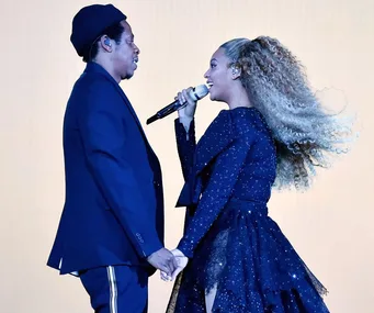 A man and a woman hold hands while performing on stage, the woman sings into a microphone.