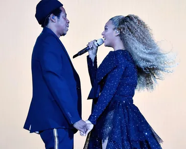 A man and a woman hold hands while performing on stage, the woman sings into a microphone.