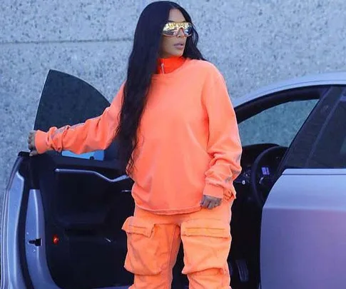 A woman in an orange outfit and reflective sunglasses steps out of a car, as part of a Yeezy campaign.