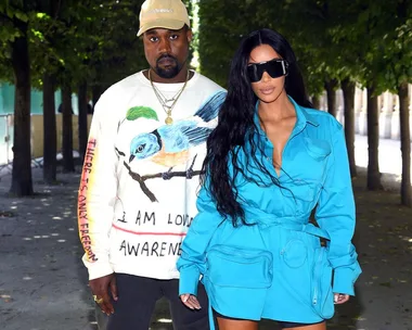 A man wearing a beige cap and white shirt with a bird graphic stands beside a woman in a blue outfit with sunglasses.