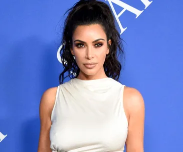 Kim Kardashian in a white dress, posing against a blue background at the CFDA Awards.