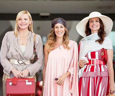 The characters Samantha, Carrie, and Charlotte from "Sex and the City" in stylish outfits, smiling together.