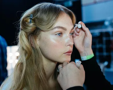 A makeup artist applies eye makeup to a woman's eyes.