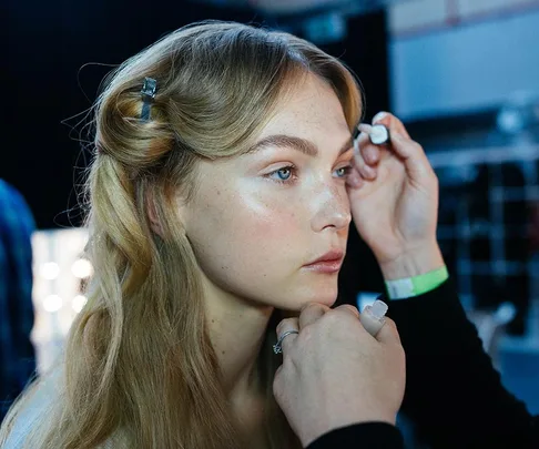 A makeup artist applies eye makeup to a woman's eyes.