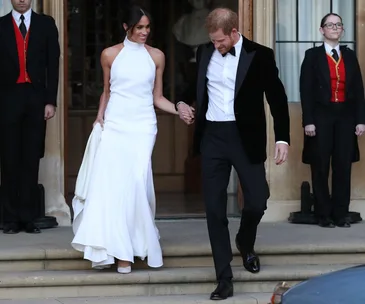 Meghan Markle in a halter-neck white dress holding Prince Harry's hand at their wedding reception.