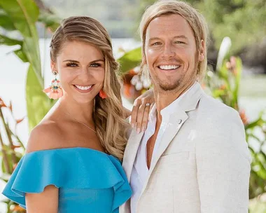 A smiling couple in colorful summer attire standing outdoors with lush greenery in the background.