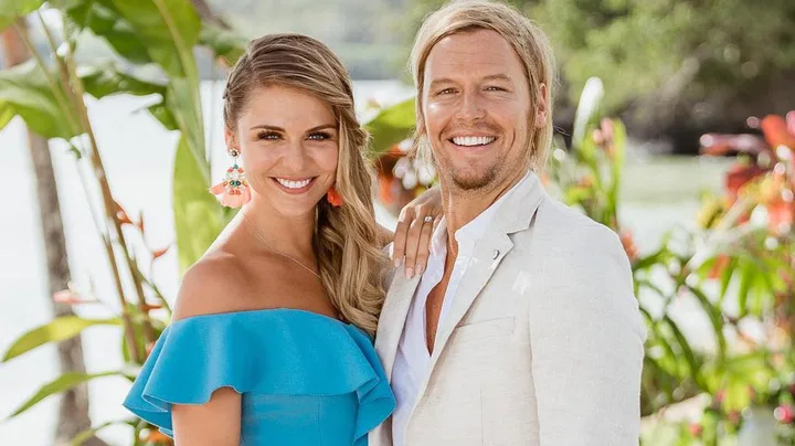 A smiling couple in colorful summer attire standing outdoors with lush greenery in the background.