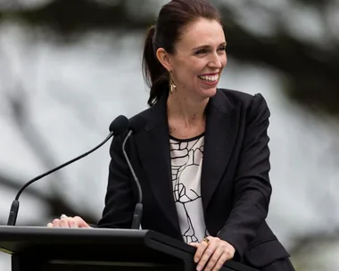 A woman in a blazer smiles while speaking at a podium with a microphone.