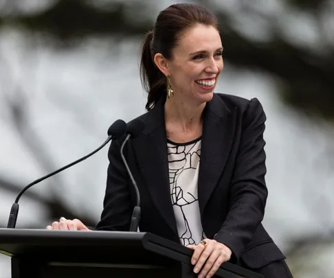 A woman in a blazer smiles while speaking at a podium with a microphone.