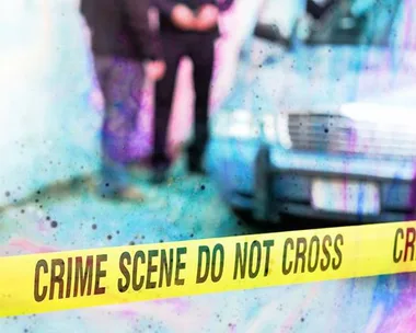 "Crime scene tape reading 'CRIME SCENE DO NOT CROSS' in front of a blurred background with two people and a car."