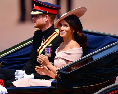 Prince Harry and Meghan Markle ride in a carriage at Trooping the Colour, Harry in military uniform and Meghan in a light pink outfit.