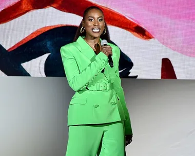 Issa Rae in a vibrant green suit, speaking on stage at the CFDA event.