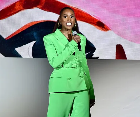 Issa Rae in a vibrant green suit, speaking on stage at the CFDA event.