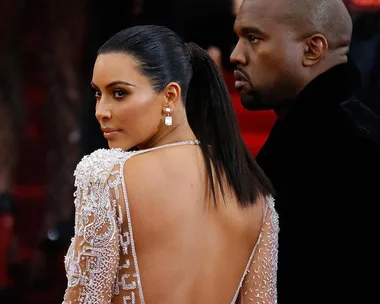 Kim Kardashian and Kanye West pose together on a red carpet, with Kardashian in a backless dress.