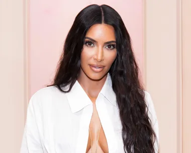 A woman with long, dark hair wearing a white, open-collared shirt, looking directly at the camera against a neutral background.