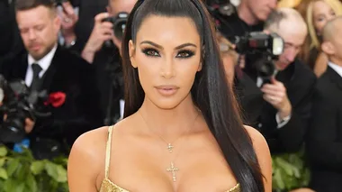 A woman in a glamorous gold dress with straight long hair attends a formal event, surrounded by photographers.