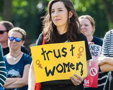 A woman holds a "Trust Women" sign during a protest regarding abortion clinics.