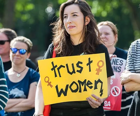 A woman holds a "Trust Women" sign during a protest regarding abortion clinics.