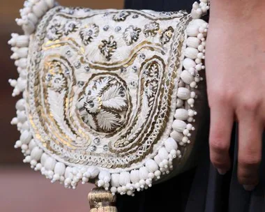 Hand carrying an intricately embroidered white and gold clutch with bead detailing.