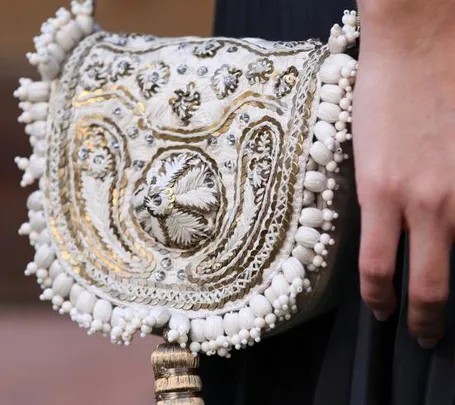 Hand carrying an intricately embroidered white and gold clutch with bead detailing.