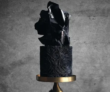 Black wedding cake with intricate swirls and a bold, abstract black topper on a gold stand.