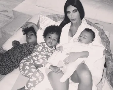 A woman lying on a couch with three young children, all in pajamas, in a cozy family moment.