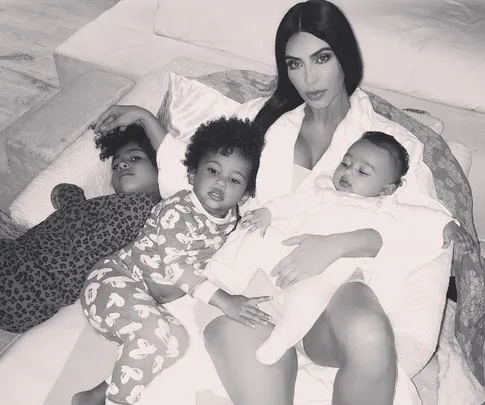 A woman lying on a couch with three young children, all in pajamas, in a cozy family moment.