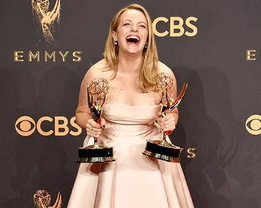 Actress in a pink dress holding two Emmy Awards, smiling widely at the 2018 Emmy Awards event.