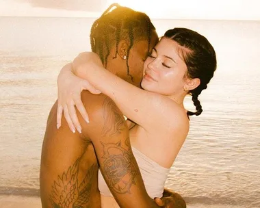 A couple hugging on the beach at sunset, with the ocean in the background.