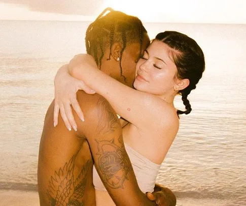 A couple hugging on the beach at sunset, with the ocean in the background.