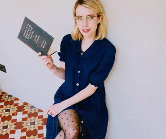 Woman in blue dress holding a book with text, sitting on a patterned floor.