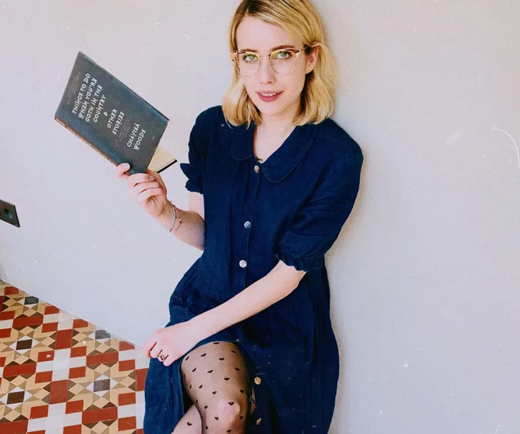 Woman in blue dress holding a book with text, sitting on a patterned floor.