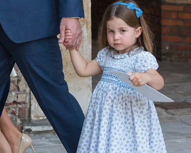 Young girl in a blue floral dress holding a man's hand and a paper during a christening event.