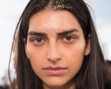 Woman with dark hair wearing biodegradable glitter on her forehead and hair at a festival.