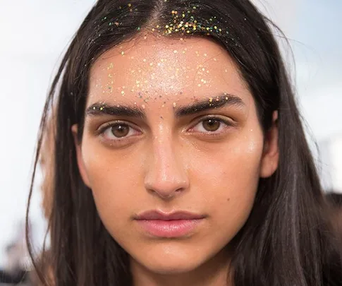 Woman with dark hair wearing biodegradable glitter on her forehead and hair at a festival.