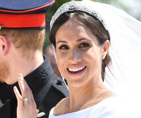 Meghan Markle in wedding dress and tiara, smiling, with Prince Harry in uniform, partially visible.