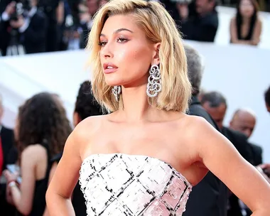 A fashionable woman in a strapless white dress and large earrings poses confidently on a red carpet.