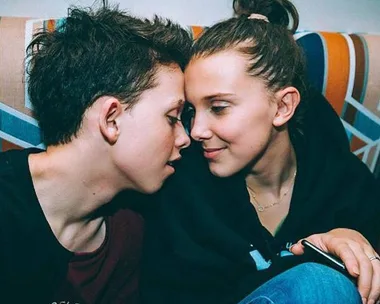 Two teenagers seated close together on a couch, leaning in with their faces almost touching, sharing an intimate moment.