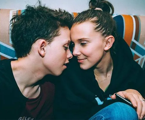 Two teenagers seated close together on a couch, leaning in with their faces almost touching, sharing an intimate moment.