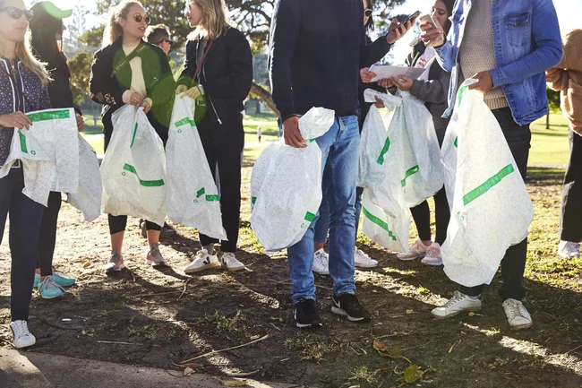 People holding reusable bags at a park, wearing casual clothing and sneakers, in an outdoor group event.
