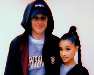 A man in a Gryffindor hoodie and black cap poses next to a woman with a long braid in a gray top and black jacket.