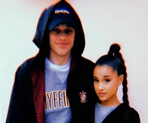 A man in a Gryffindor hoodie and black cap poses next to a woman with a long braid in a gray top and black jacket.