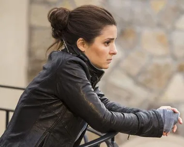 Woman in leather jacket leaning on a railing, gazing thoughtfully into the distance.