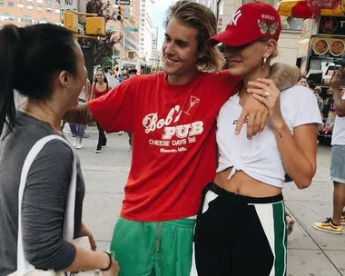 A man in a red shirt and a woman in a red cap pose smiling with another woman on a busy city street.